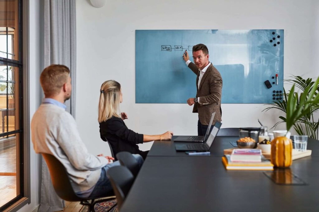 Möte i mötesrum där man visar flödesschema på whiteboard